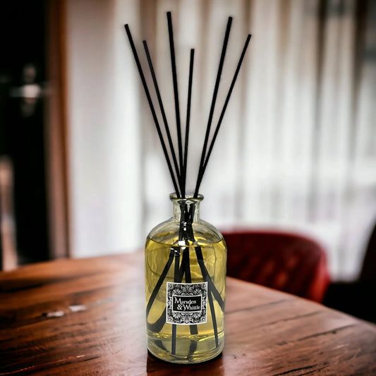 Reed diffuser with black sticks in a glass bottle on a wooden table.