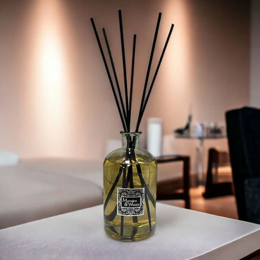 Large reed diffuser with black reeds in a glass bottle on a table in a living room setting.
