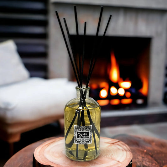 Reed diffuser bottle with decorative sticks on a wooden coaster in front of a fireplace.