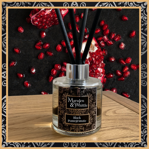 A Black Pomegranate glass reed diffuser with black reeds and a silver chrome cap sitting on a wooden table.