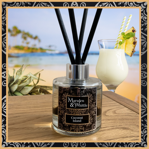 A Coconut Island glass reed diffuser with black reeds and a silver chrome cap sitting on a wooden table.