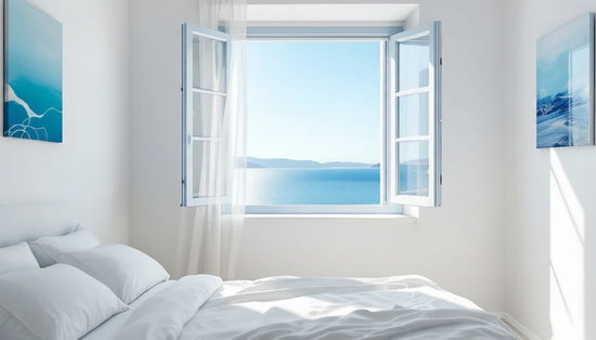 Open window in a bedroom with a view of water, white bedding, and two framed artworks.