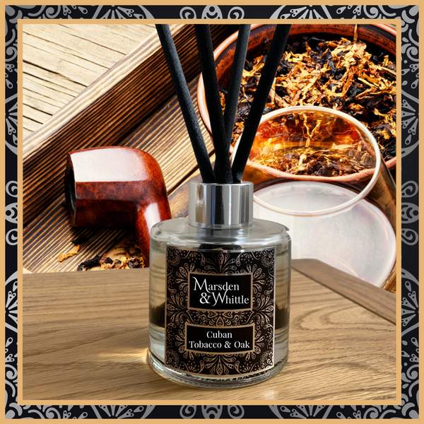 A Cuban Tobacco & Oak glass reed diffuser with black reeds and a silver chrome cap sitting on a wooden table.