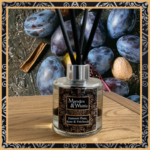 A Damson Plum, Rose and Patchouli glass reed diffuser with black reeds and a silver chrome cap sitting on a wooden table.