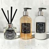 A Damson Plum, Rose & Patchouli Reed Diffuser, Hand & Body Wash and Hand & Body Lotion sitting on a white marble surface with a white marble splash back behind.