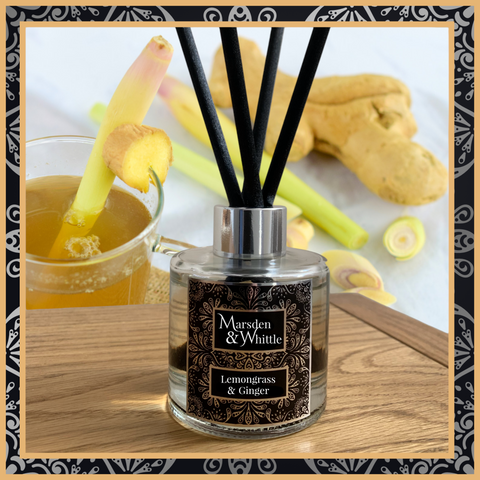 A Lemongrass and Ginger glass reed diffuser with black reeds and a silver chrome cap sitting on a wooden table.
