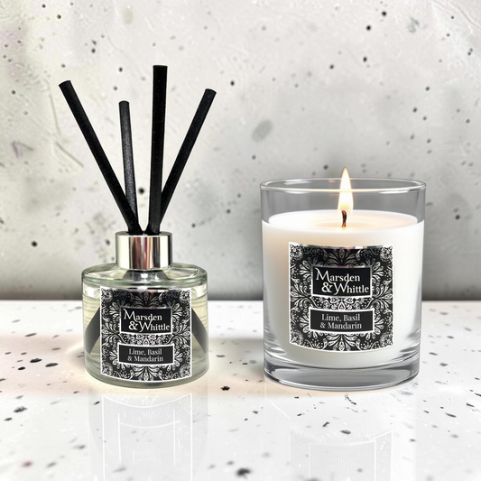 A reed diffuser and a lit scented candle from the brand Marsden & Whittle, both labeled 'Lime, Basil & Mandarin,' displayed on a light speckled surface against a textured light gray wall.