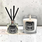 A reed diffuser and a lit scented candle from the brand Marsden & Whittle, both labeled 'Myrrh & Tonka' displayed on a light speckled surface against a textured light gray wall.