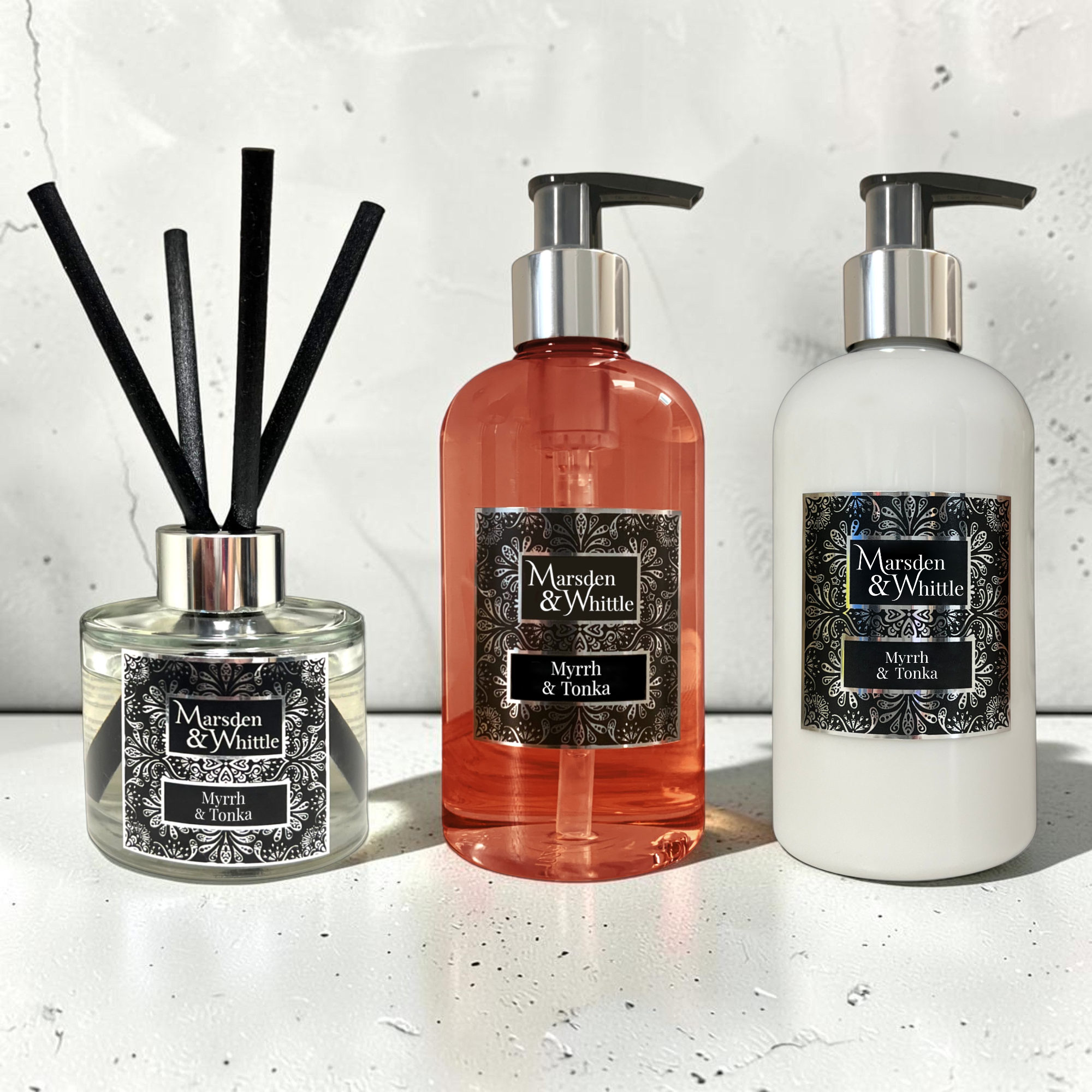 A Myrrh & Tonka Reed Diffuser, Hand & Body Wash and Hand & Body Lotion sitting on a white marble surface with a white marble splash back behind.