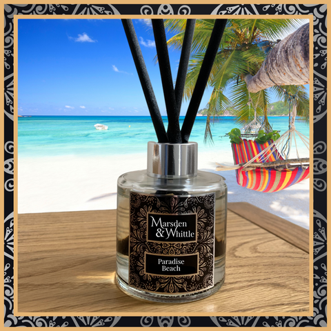 A Paradise Beach glass reed diffuser with black reeds and a silver chrome cap sitting on a wooden table.