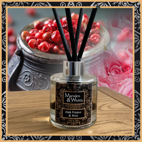 A Pink Pepper and Rose glass reed diffuser with black reeds and a silver chrome cap sitting on a wooden table.