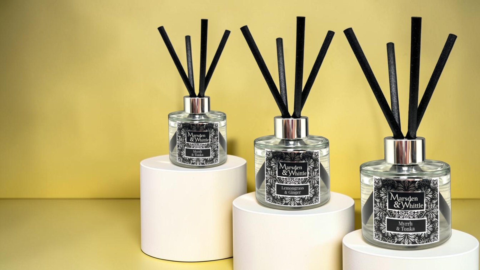 Three Marsden & Whittle EReed Diffusers sat elegantly on plinths, two Myrrh & Tonka and one Lemongrass & Ginger. The background is light yellow and the plinths are a soft light cream.