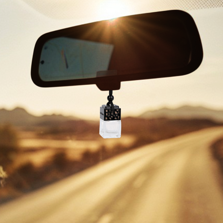 Car rearview mirror with a Marsden & Whittle Car Diffuser hanging from it, set against a scenic road backdrop.