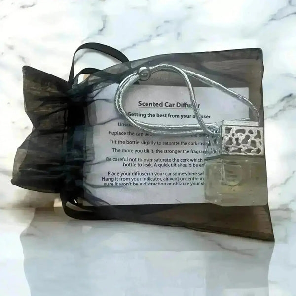 A glass car diffuser with silver lid in a black organza draw-string bag