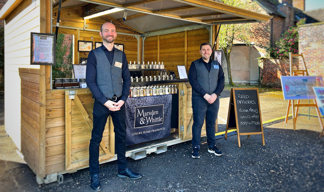 Matt and Scott standing outside the Marsden & Whittle wooden chalet in their smart uniforms.