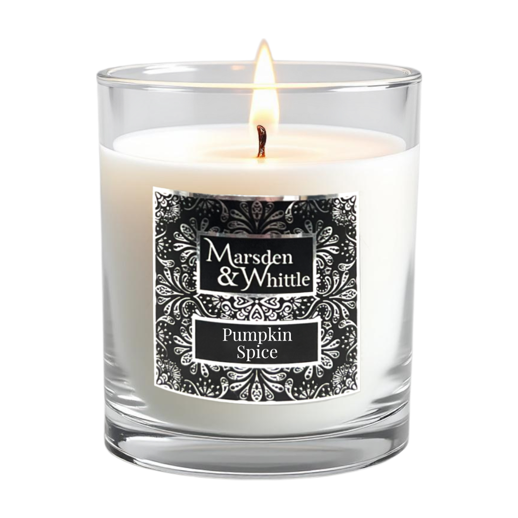 A lit white candle in a clear glass jar with a black and chrome ornate label reading 'Marsden & Whittle' and 'Pumpkin Spice'.