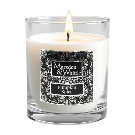 A lit white candle in a clear glass jar with a black and chrome ornate label reading 'Marsden & Whittle' and 'Pumpkin Spice'.