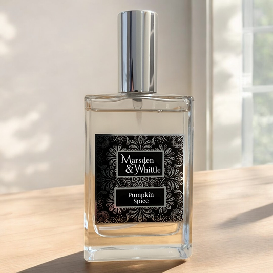 A rectangular glass spray bottle with a silver cap and a black patterned label reading 'Marsden & Whittle' and 'Pumpkin Spice', placed on a wooden surface in soft natural light.