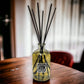 Reed diffuser with black sticks in a glass bottle on a wooden table.