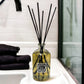 Large reed diffuser with black reeds in a glass bottle on a bathroom counter.