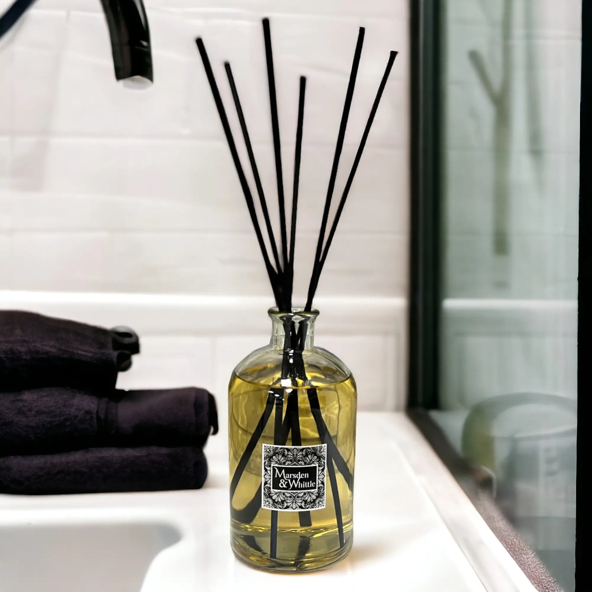 Large reed diffuser with black reeds in a glass bottle on a bathroom counter.