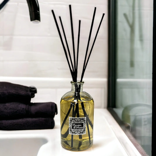 Large reed diffuser with black reeds in a glass bottle on a bathroom counter.