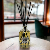 Large diffuser bottle with black reeds on a table in a blurred indoor setting